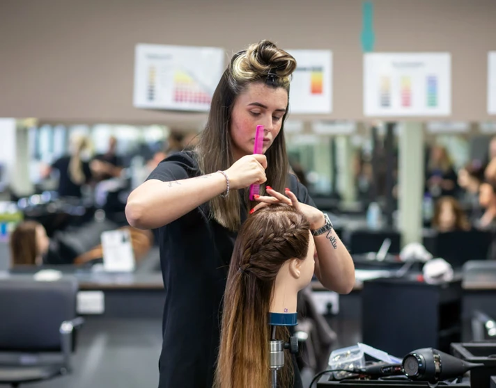 Hairstyling student carefully styling a mannequin’s hair in a salon. Hairstyling student carefully styling a mannequin’s hair in a salon.